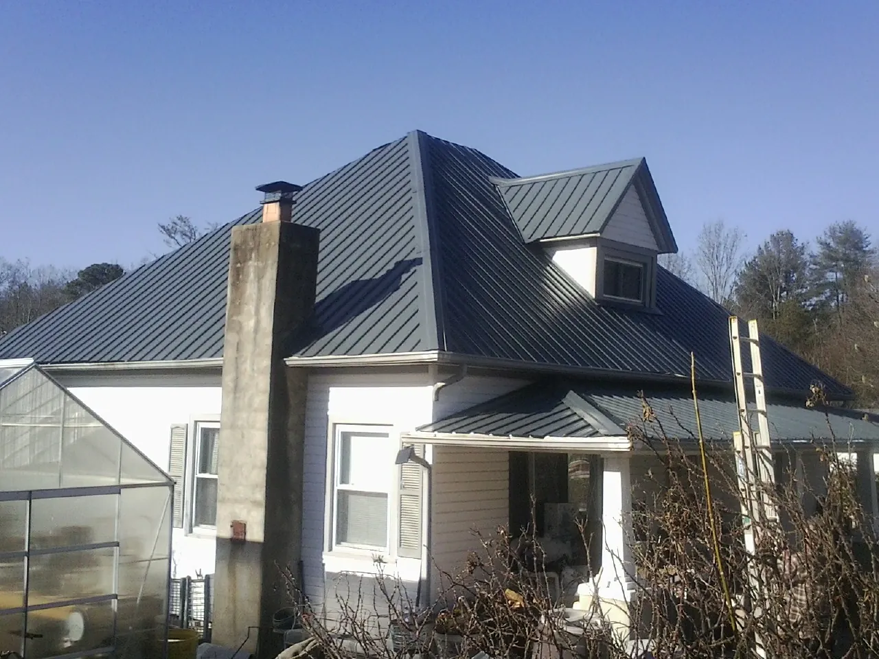 Dark blue standing seam metal roof on a white farmhouse with dormer — Slate & Tile Roof Repair by Roofing Brothers in Sweet Valley