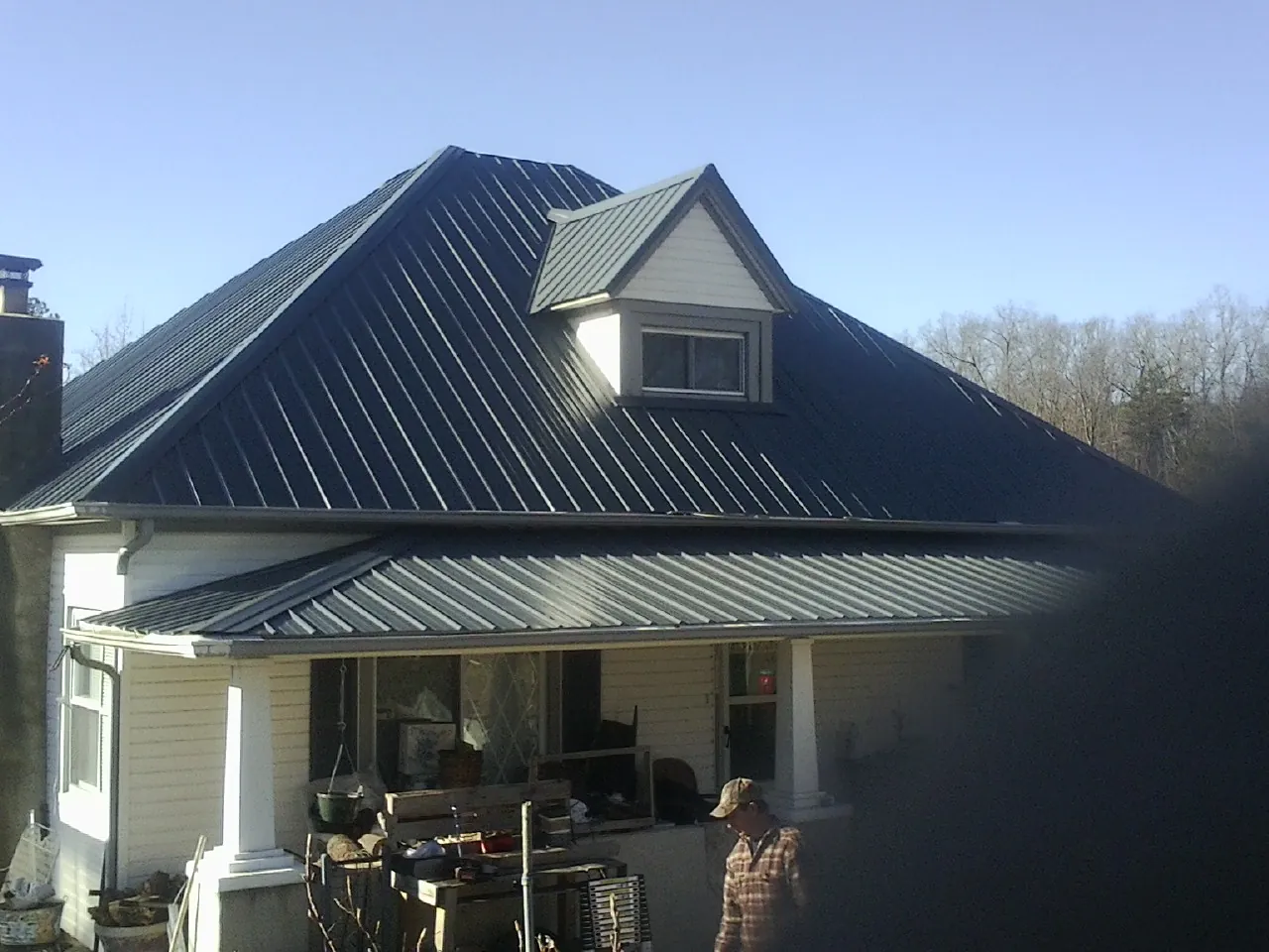 Dark blue standing seam metal roof with a dormer above a front porch in Sweet Valley