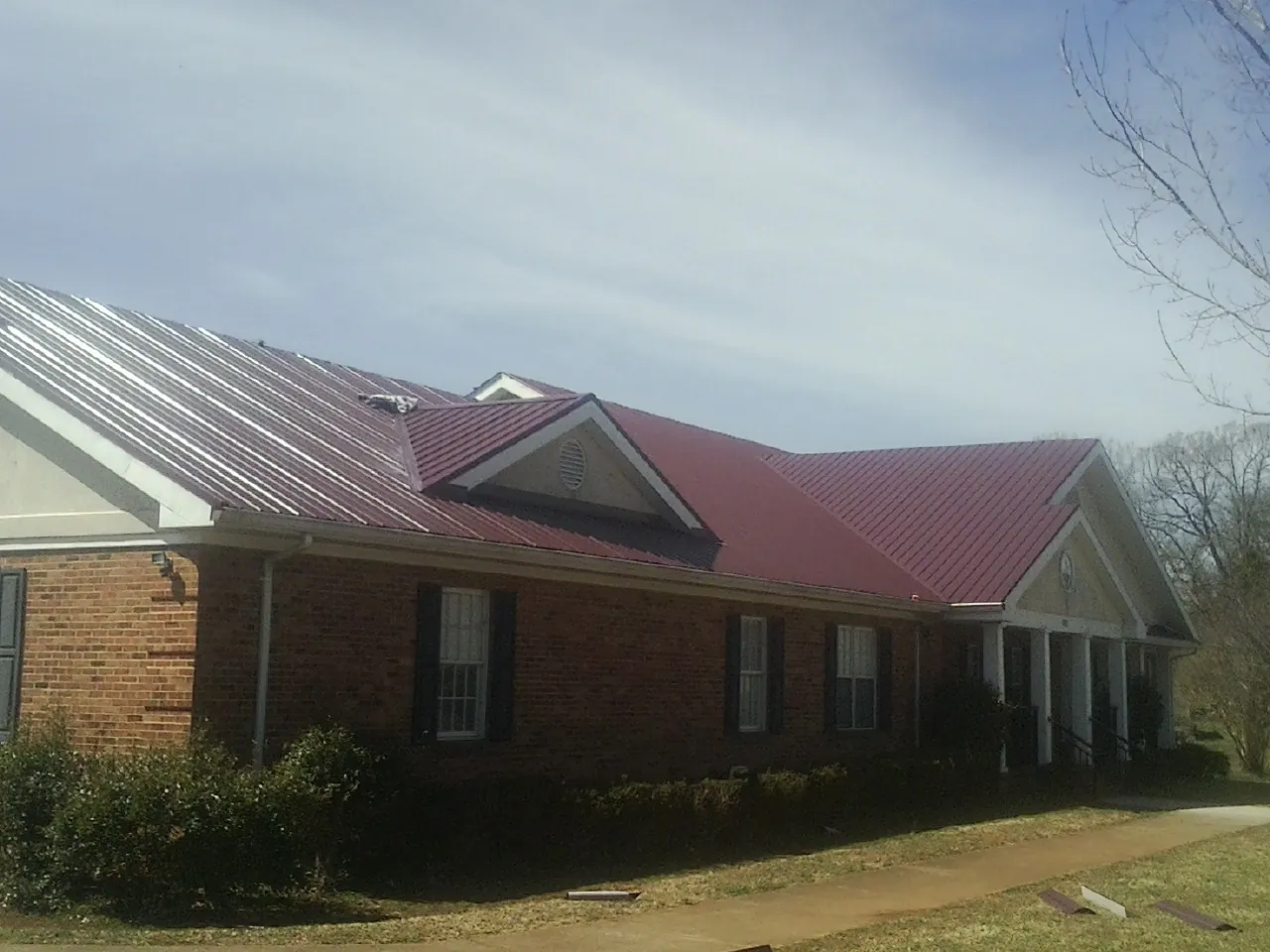 Red metal roof with gabled entries on a long brick building, from a Hail Damage Roof Repair job in Sweet Valley