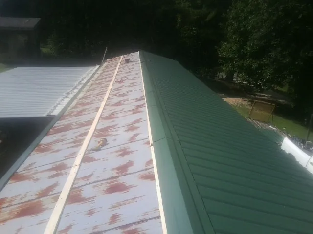 Old rusted panels beside newly installed green metal roofing — Wind Damage Roof Repair by Roofing Brothers in Sweet Valley
