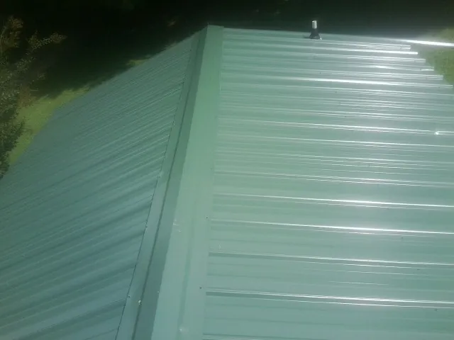 New green metal panels meeting at the ridge of a roof — Flat Roof Repair work by our crew in Sweet Valley