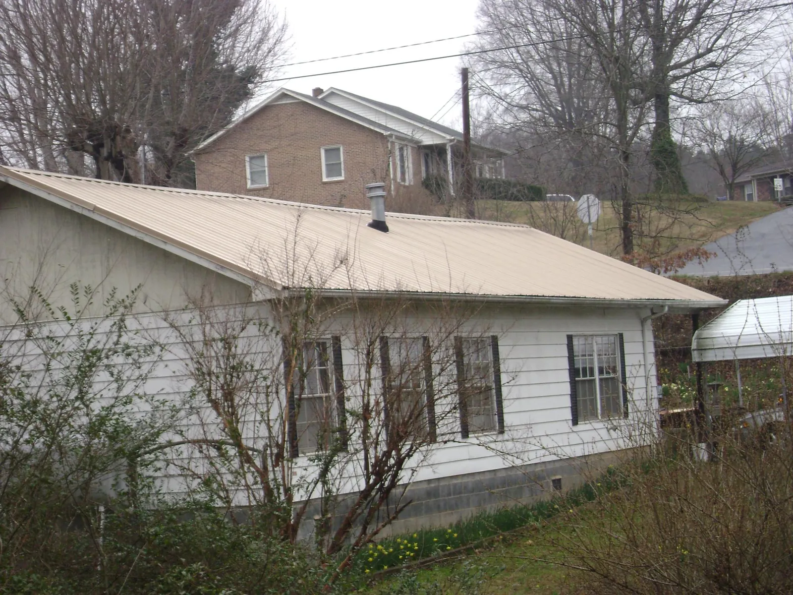 Tan metal roof on a white sided house set into a hillside — Commercial Roofing by Roofing Brothers in Sweet Valley